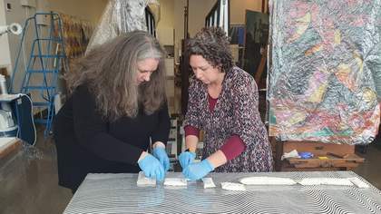 Two women wearing gloves cleaning a painting.