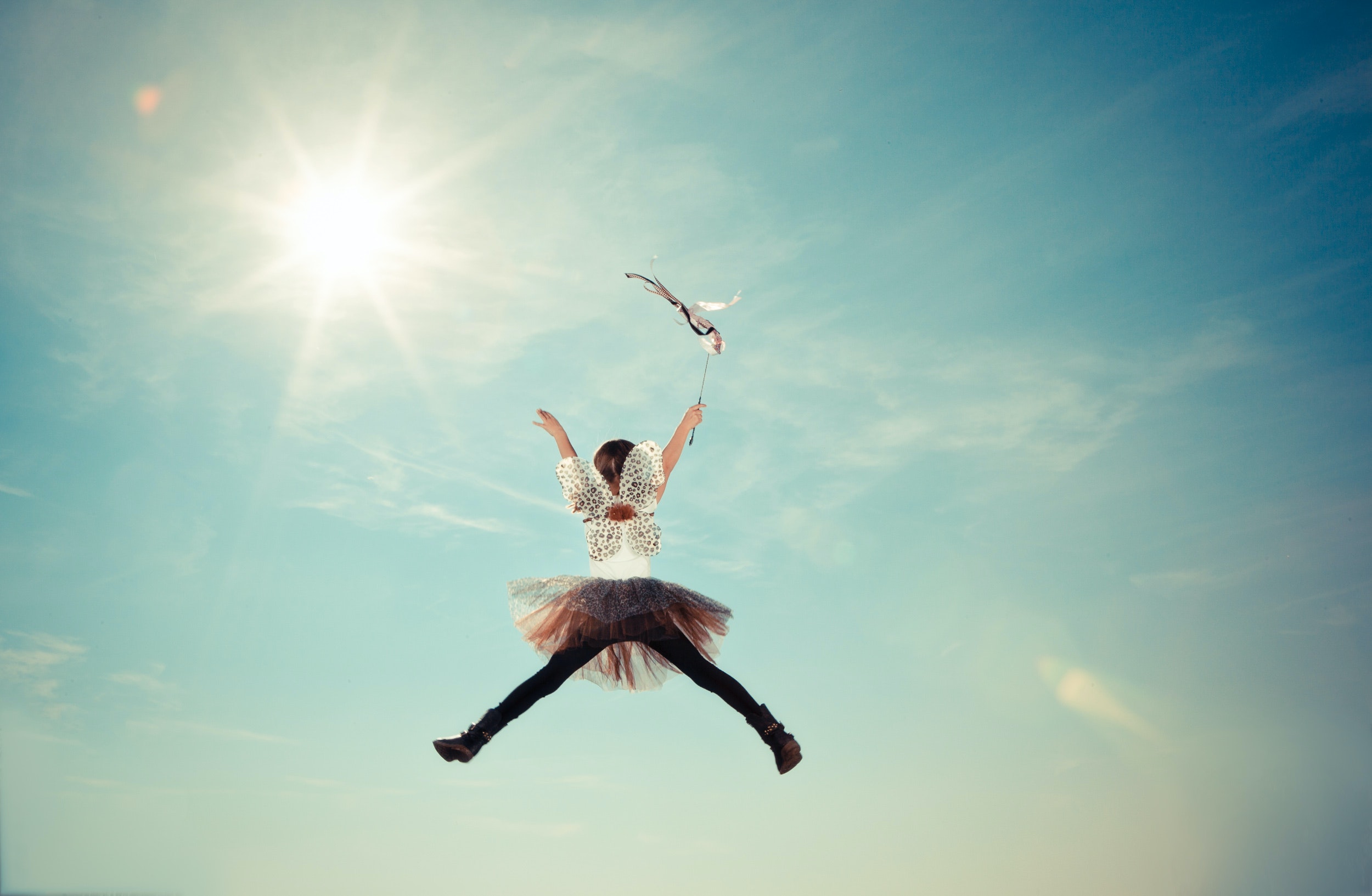 A girl dressed in fairy wings jumps in the sky